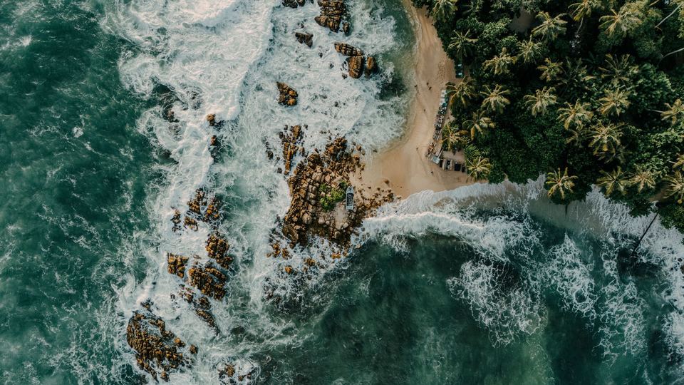 Ralla: the reef from above, surf breaking white over dark rock and sand.